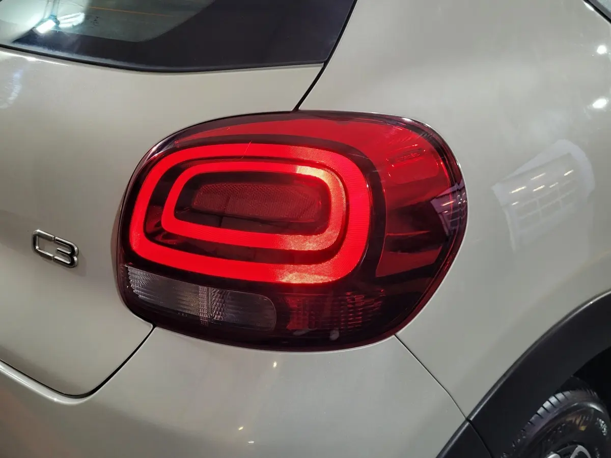 Feu arrière droit allumé sur une Citroën C3 beige vue de près, avec logo C3 visible sur la carrosserie.