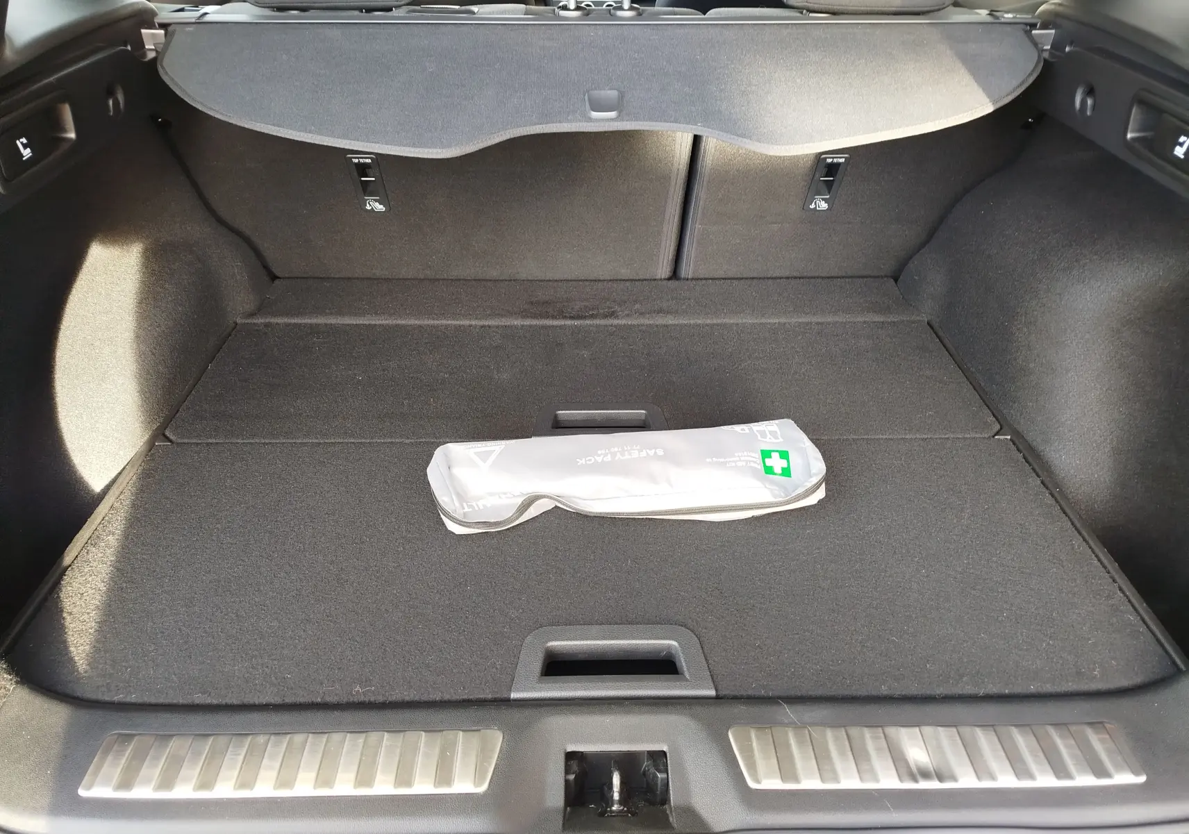 Coffre ouvert vu de l'arrière du Renault Kadjar gris titanium, avec une trousse de sécurité posée au centre.