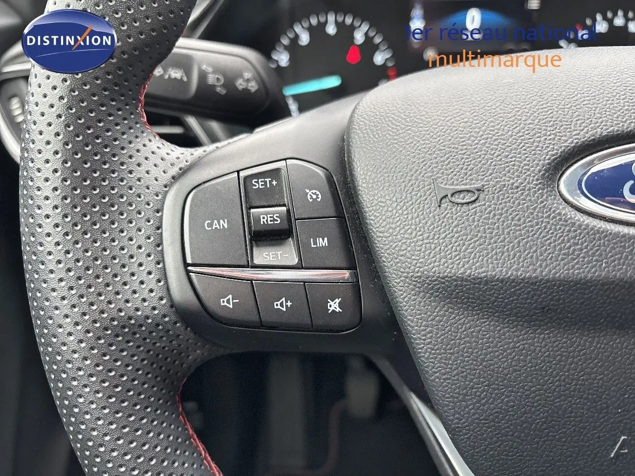 Gros plan sur le volant perforé avec commandes intégrées du Ford Puma gris Solar, tableau de bord flou en arrière-plan.