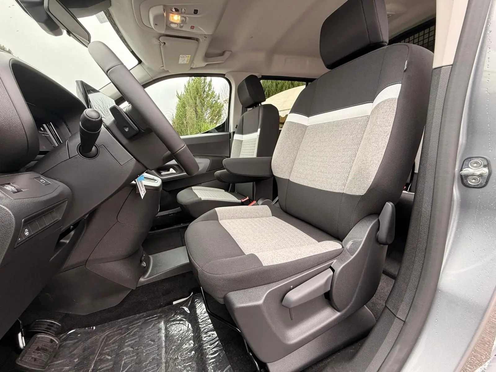 Vue intérieure côté conducteur du Citroën Berlingo gris Artense, sièges tissu bicolore gris et noir avec accoudoir.