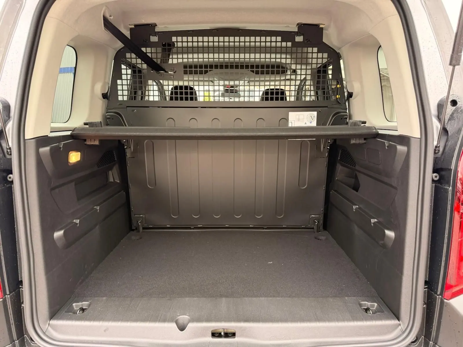 Vue arrière du coffre spacieux du Citroën Berlingo gris, avec séparation métallique et tablette de rangement.