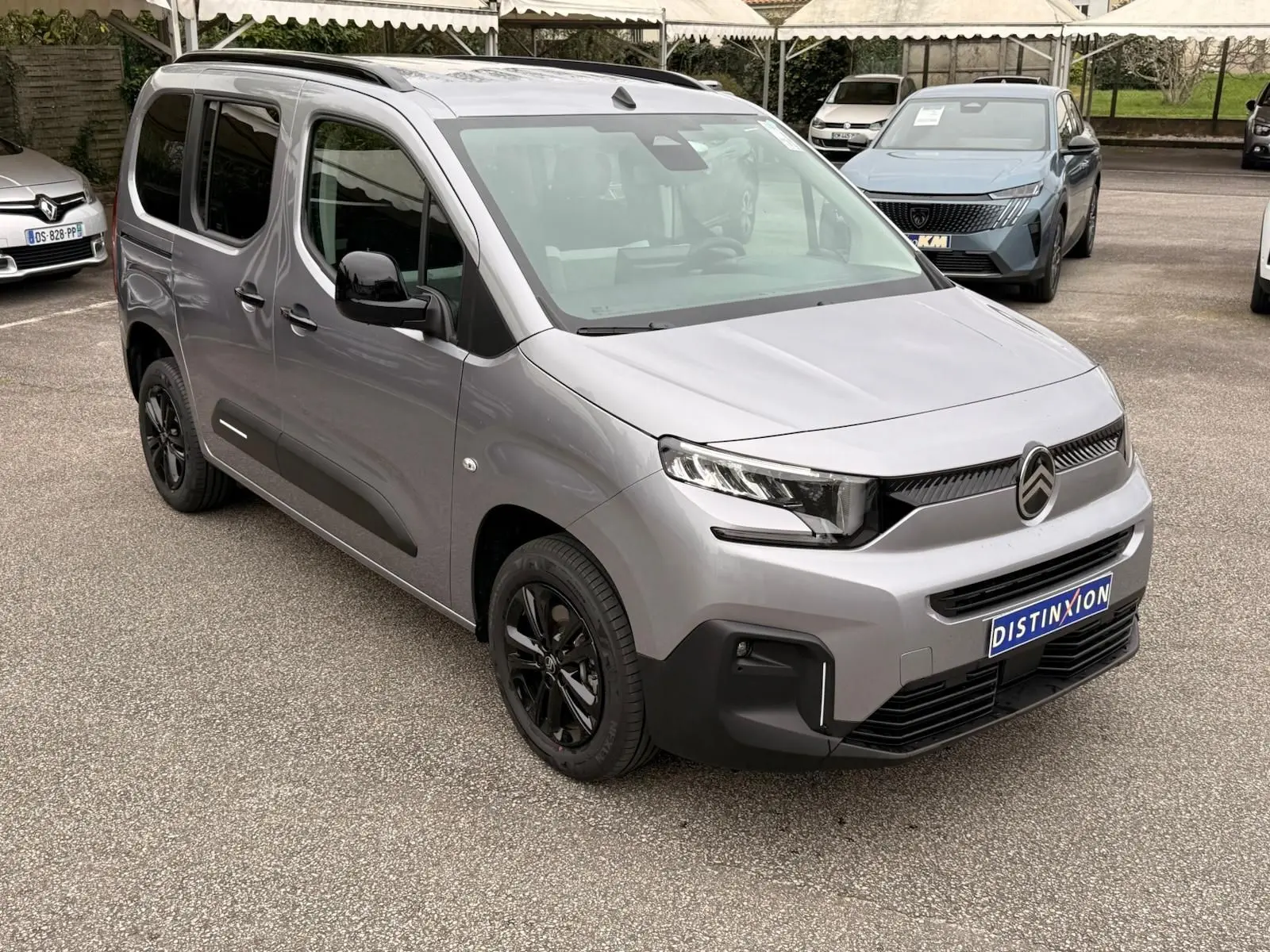 Vue 3/4 avant droit d'un Citroën Berlingo gris Artense 2025 avec jantes noires et calandre moderne sur parking.