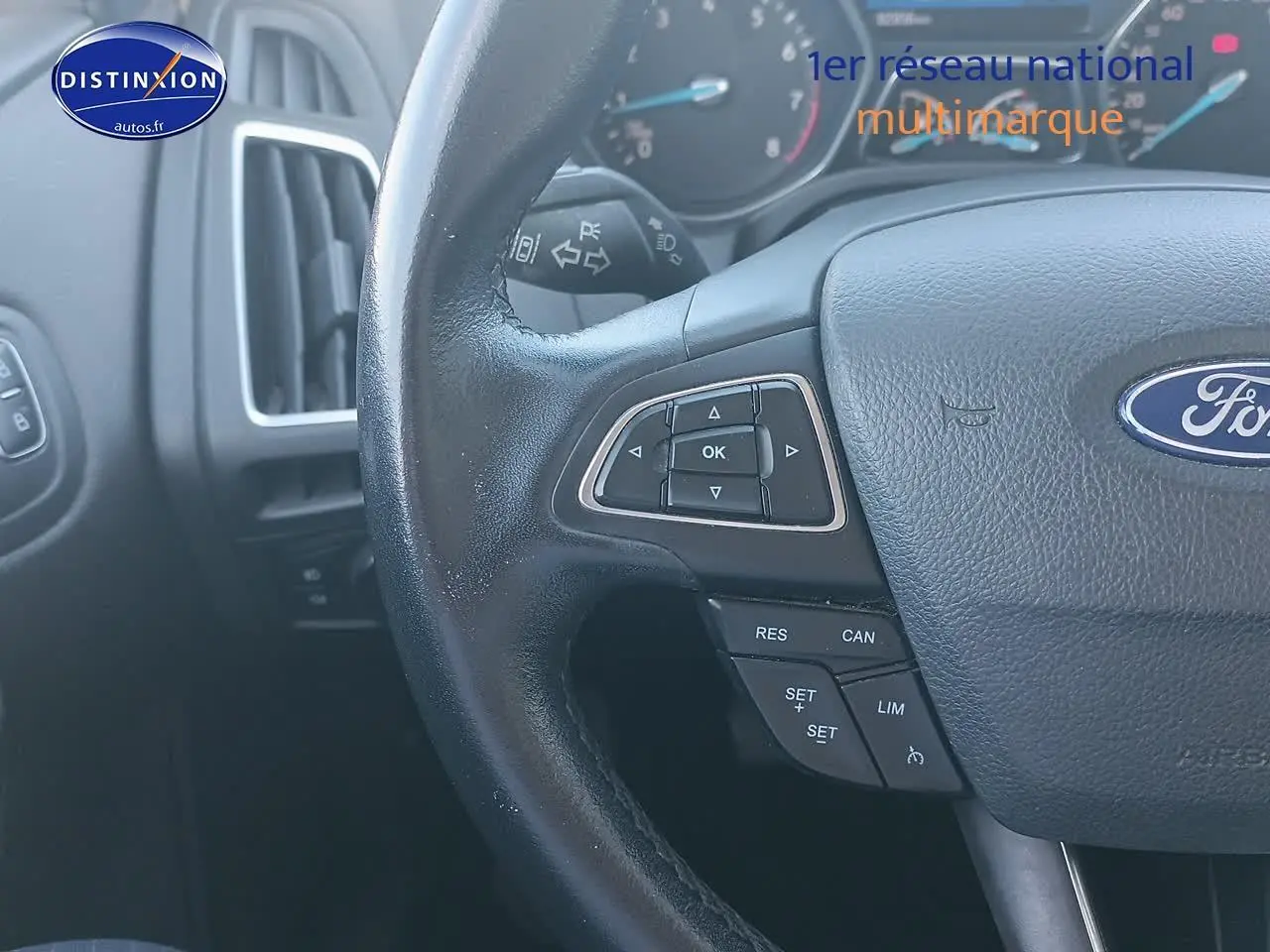 Gros plan sur le volant cuir multifonction de la Ford Focus gris clair, avec commandes au volant visibles côté gauche.