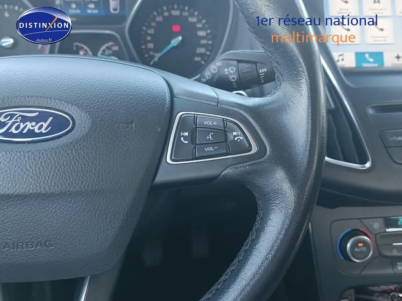 Gros plan sur le volant cuir multifonction d'une Ford Focus 2017, avec commandes audio et tableau de bord en arrière-plan.