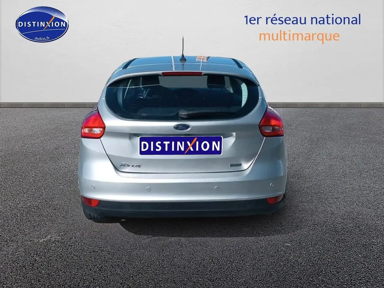 Vue arrière d'une Ford Focus gris clair 2017 avec feux rouges et logo Ford visible sur un sol goudronné.