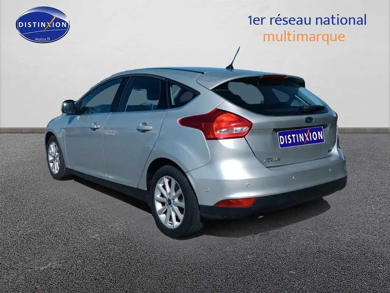 Ford Focus gris clair vue 3/4 arrière droit avec jantes alu et becquet arrière sur fond neutre.