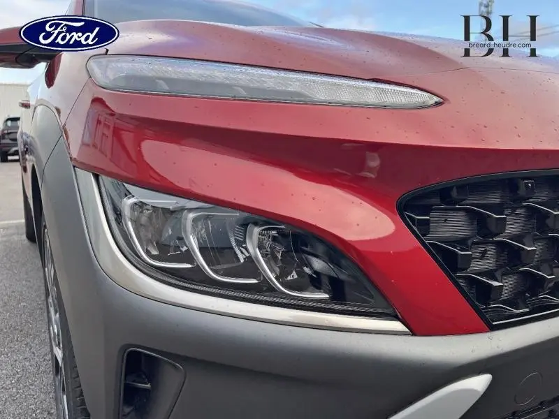 Gros plan sur le phare avant gauche rouge Pulse Red Métal du Hyundai Kona 2022 avec calandre noire et pare-chocs gris.