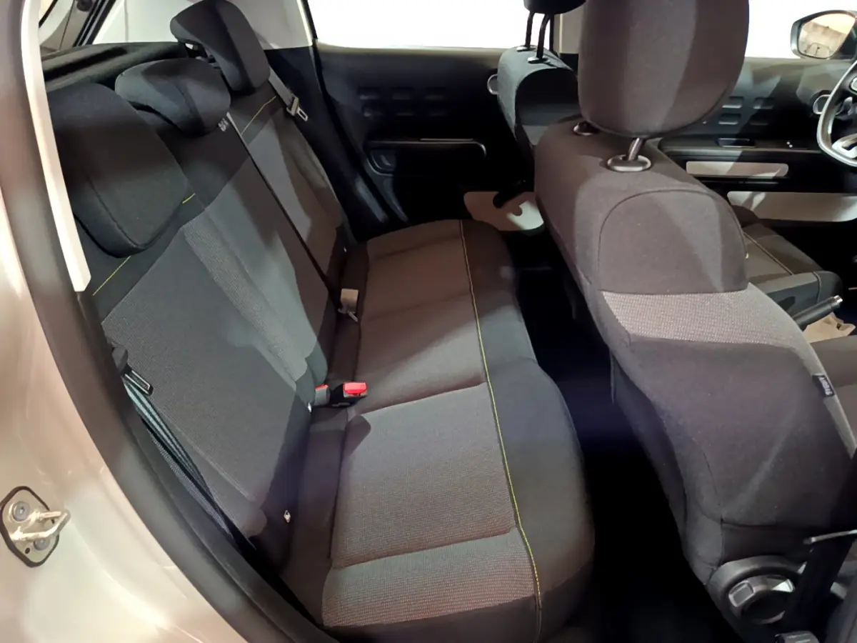Vue intérieure côté arrière gauche de la Citroën C3 beige 2022, montrant la banquette arrière et les sièges avant en tissu noir.