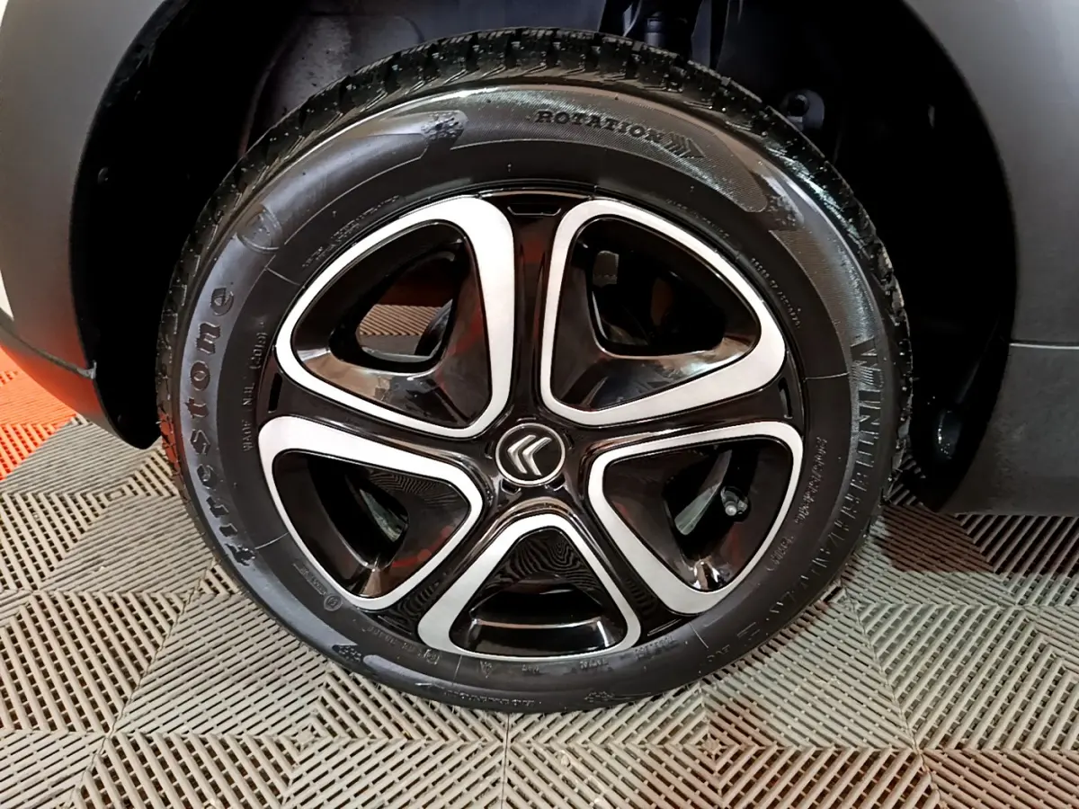 Gros plan sur la roue avant gauche avec jante alliage noire et argentée du Citroën C3 beige 2022.