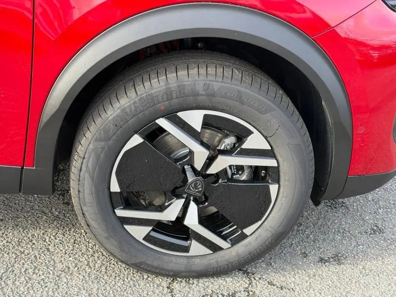 Gros plan sur la roue avant droite avec jante alu noire et argentée, entourée de la carrosserie rouge vif du Peugeot 2008.