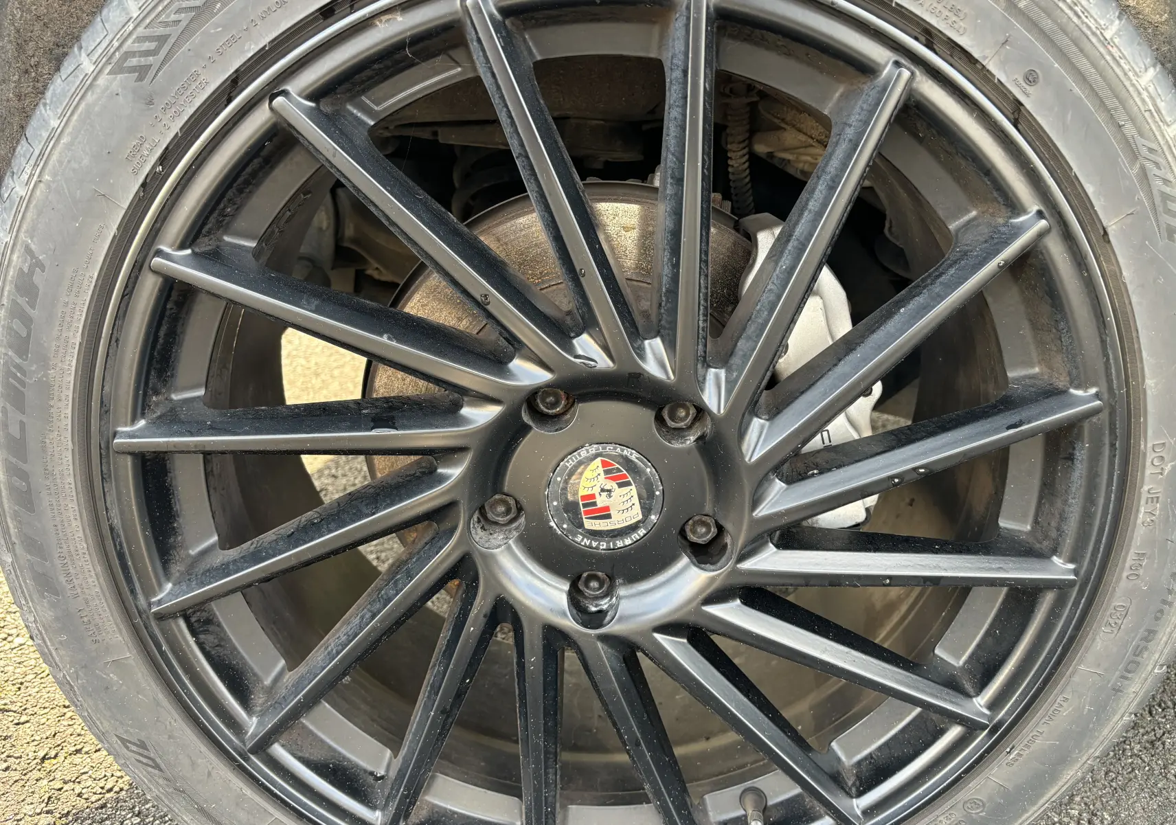 Gros plan sur la jante noire multi-branches d’un Porsche Cayenne S 4,8L V8 de 2007 avec logo Porsche au centre.