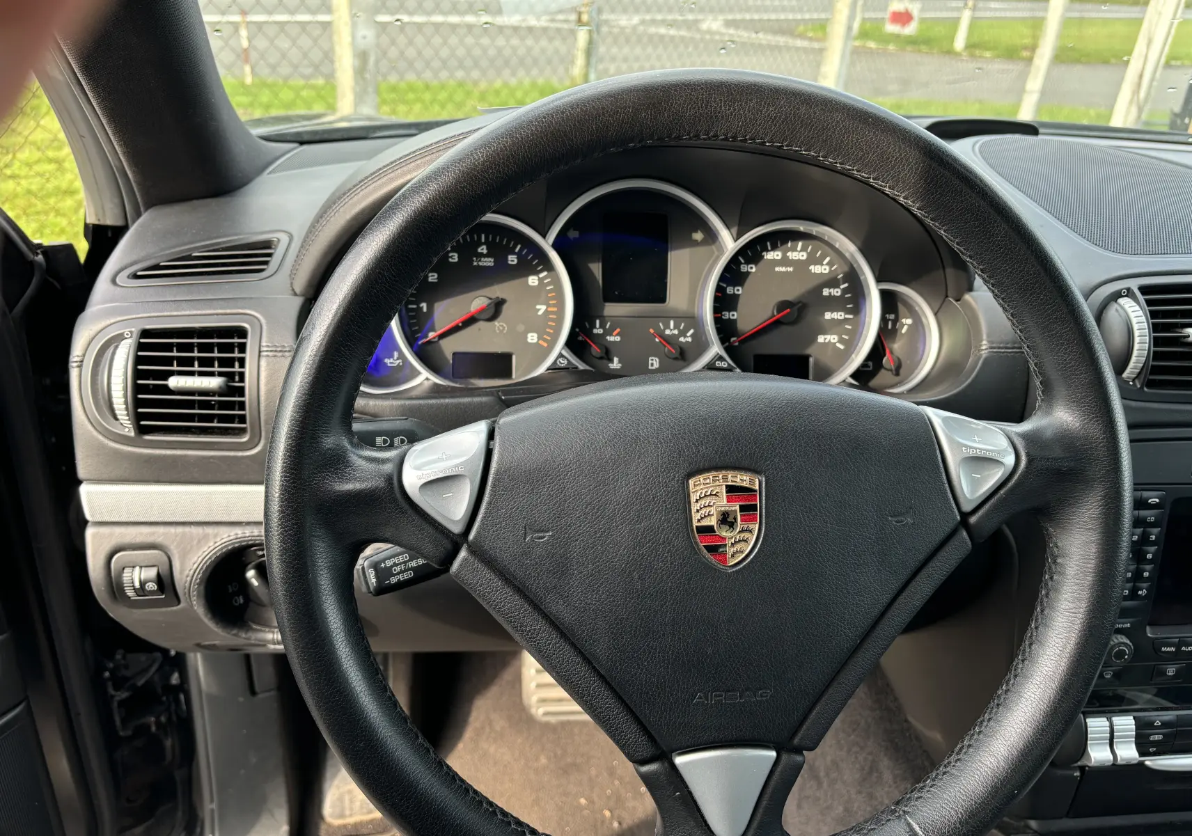 Vue rapprochée du volant en cuir noir d'une Porsche Cayenne 2007 avec tableau de bord et compteurs visibles.