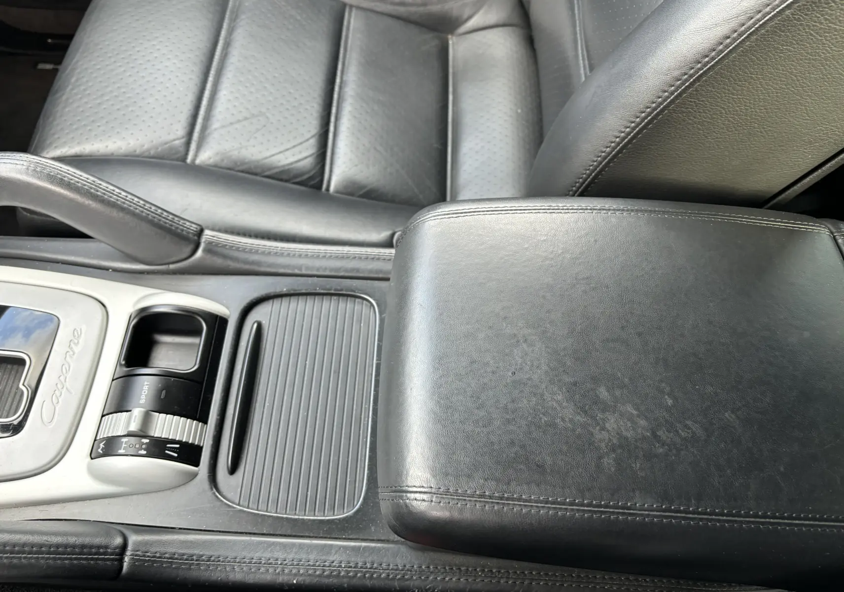 Détail de l'accoudoir central en cuir noir et console centrale avec commande de mode Sport dans une Porsche Cayenne noire.