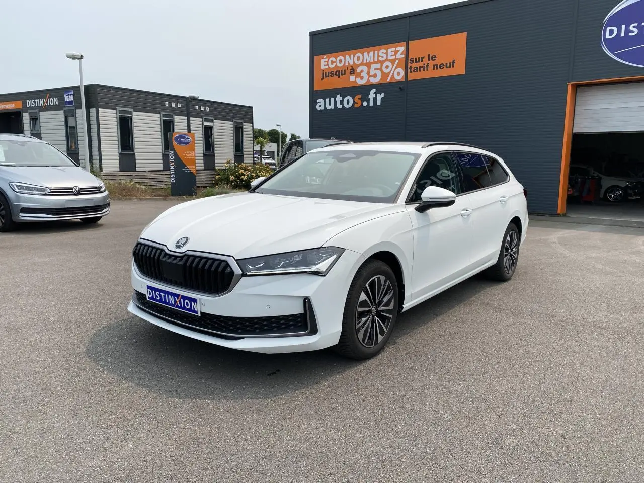 SKODA Superb Combi blanc pur en 3/4 avant droit, jantes alliage noires polies et vitres surteintées visibles.