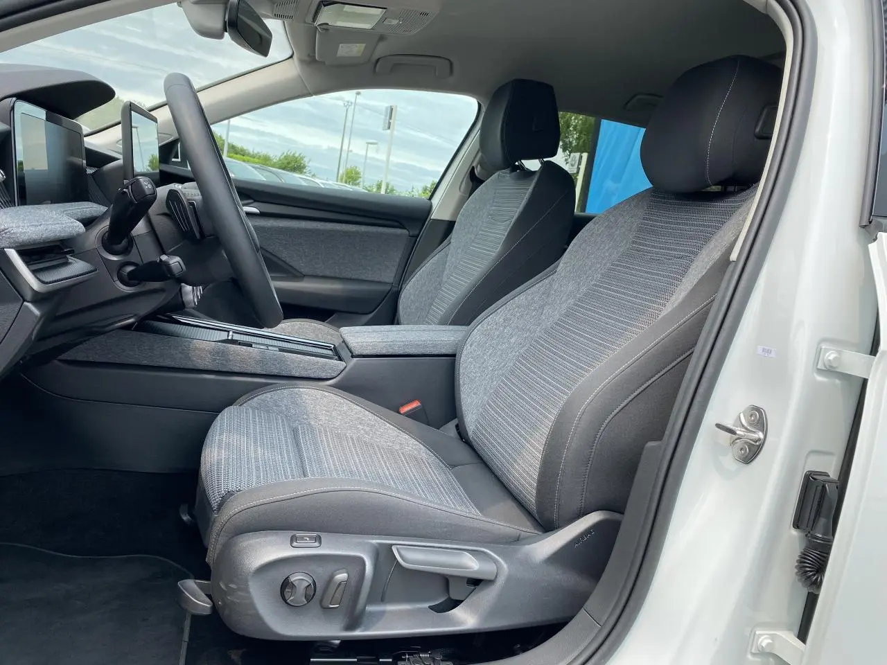 Intérieur côté conducteur de la Skoda Superb Combi blanc pure 2024, sièges tissu gris avec commandes électriques visibles.
