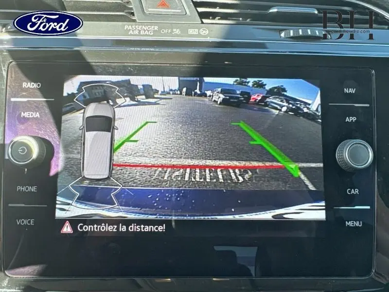 Écran de caméra de recul affichant une vue arrière avec lignes de guidage vertes et rouges sur un sol goudronné.