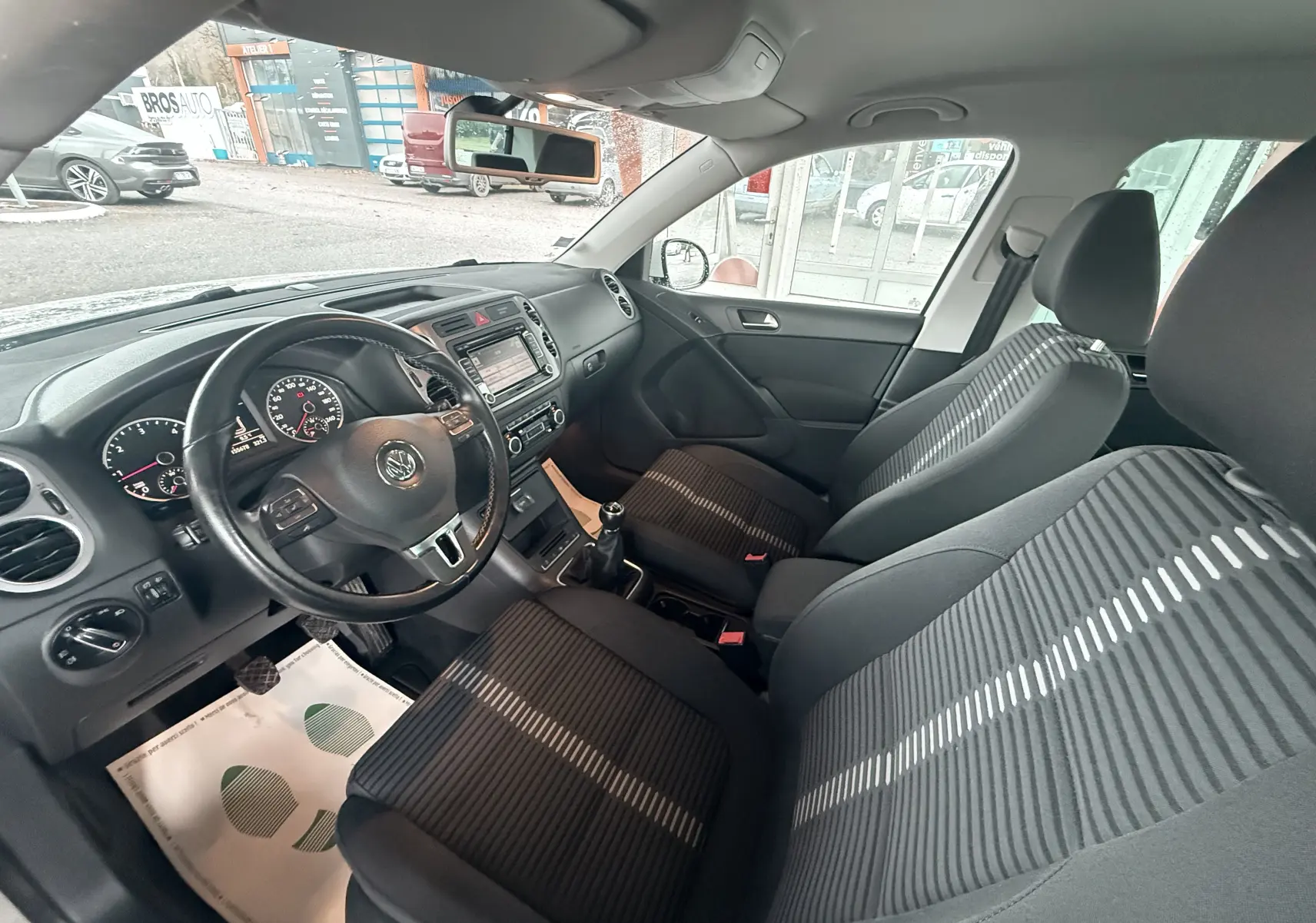 Vue intérieure côté conducteur du Volkswagen Tiguan blanc de 2010, montrant le volant cuir, tableau de bord et sièges tissu noir rayé.