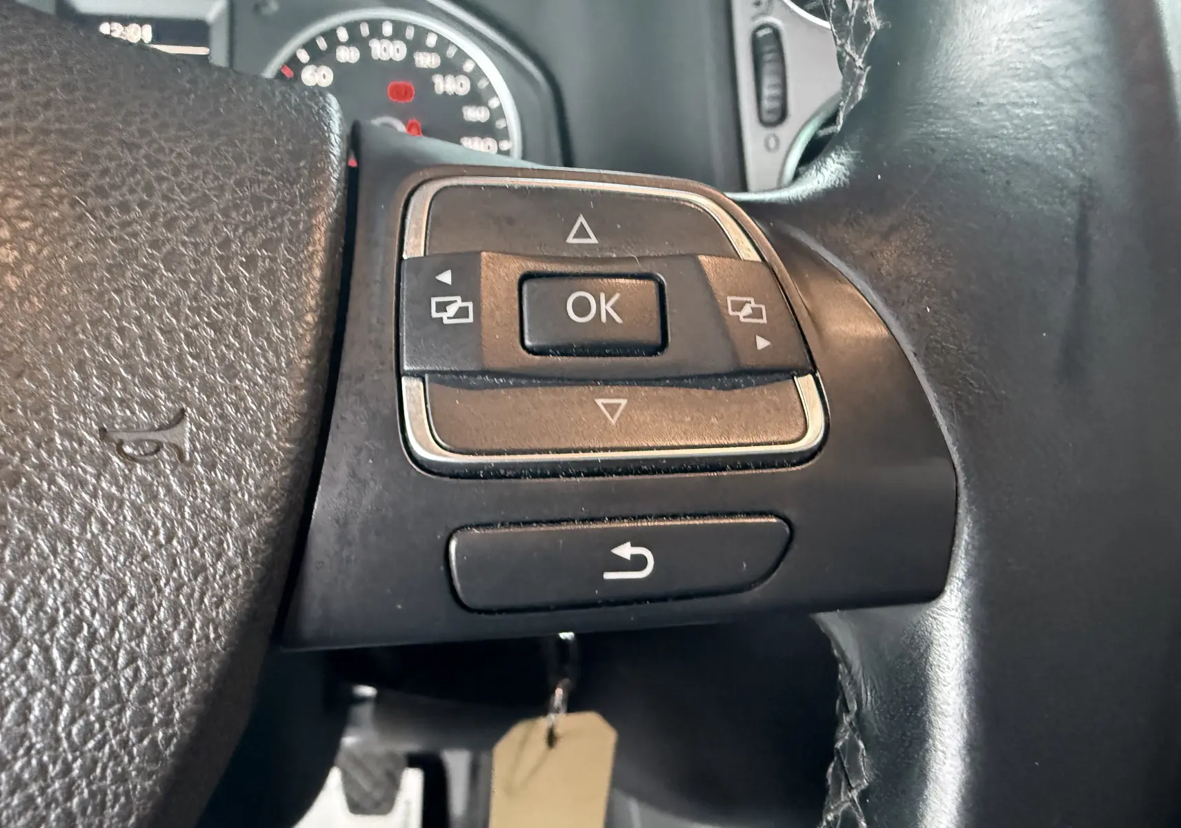 Gros plan sur les commandes gauche du volant en cuir noir du Volkswagen Tiguan 2010, avec boutons de navigation et compteur en arrière-plan.