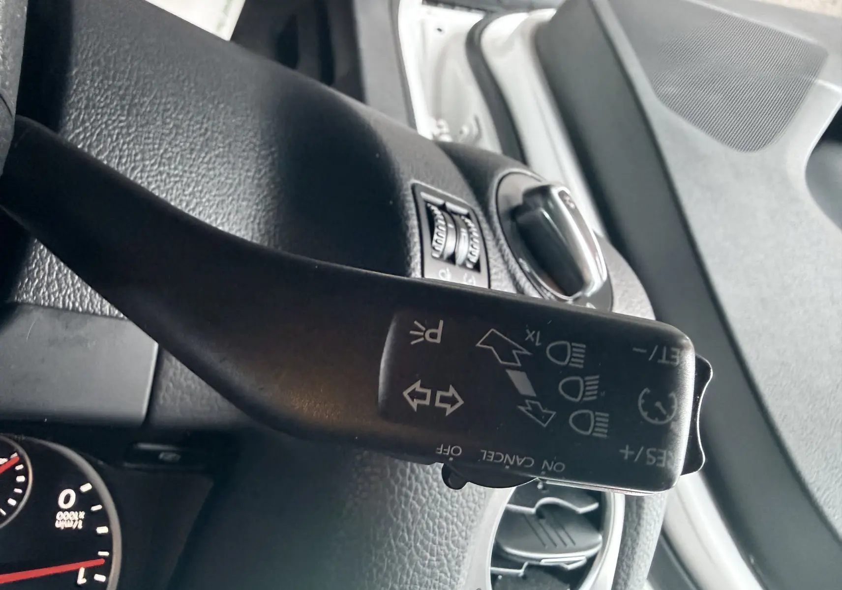 Gros plan sur le commodo de clignotants du Volkswagen Tiguan 2.0 TDI blanc, avec tableau de bord et aérateurs visibles.