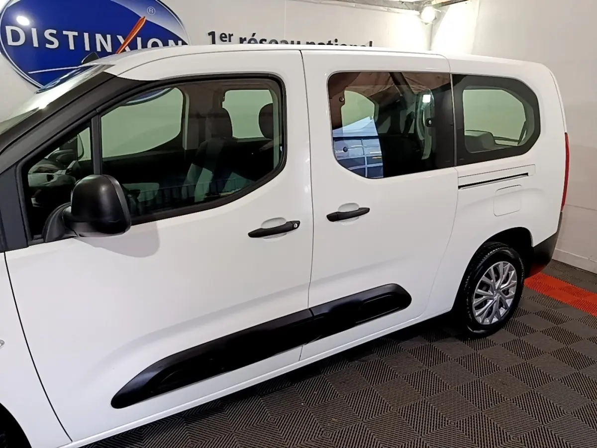 Vue de profil côté gauche d’un Citroën Berlingo XL blanc avec protections latérales noires en intérieur showroom.