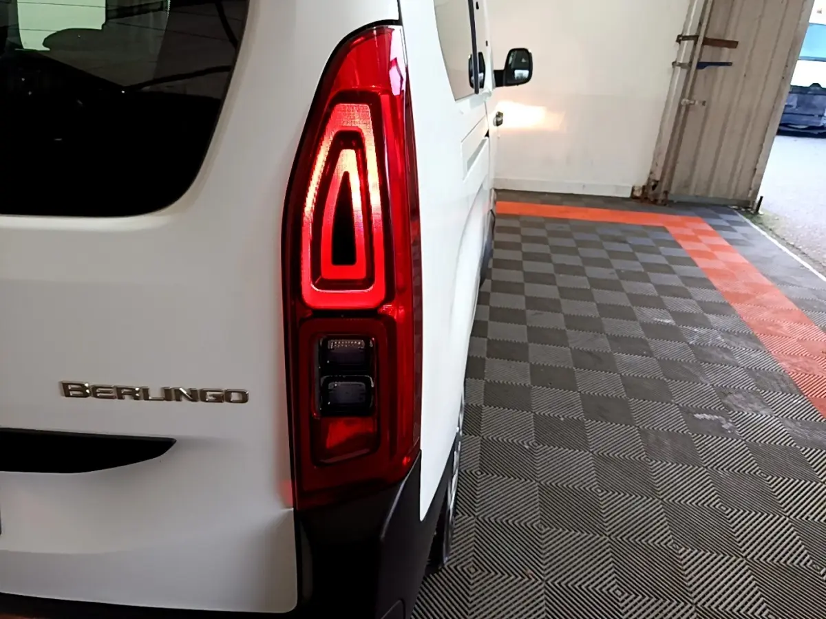 Gros plan sur le feu arrière droit rouge d’un Citroën Berlingo blanc, vue arrière côté droit dans un garage.