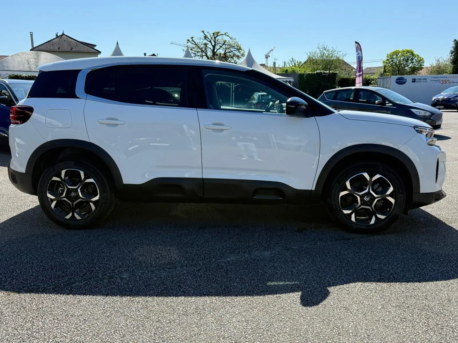 Profil côté droit d'un Citroën C5 Aircross blanc banquise avec jantes bi-ton et toit noir en extérieur.