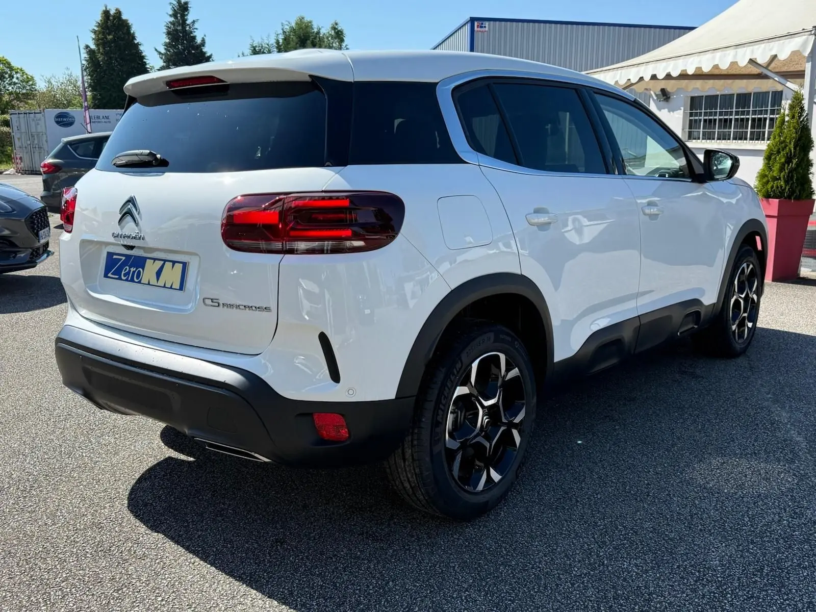 Vue 3/4 arrière droite d'un Citroën C5 Aircross blanc banquise avec jantes bi-ton et protections noires basses.