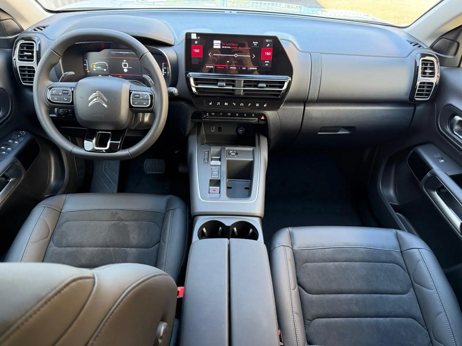 Intérieur du Citroën C5 Aircross hybride 2024 vu de face, tableau de bord moderne avec écran tactile et sièges cuir noir.