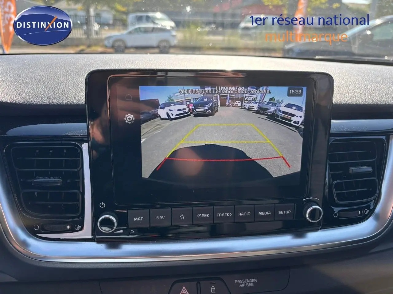 Écran central du tableau de bord du Kia Stonic 2024 montrant la caméra de recul avec vue arrière sur parking.