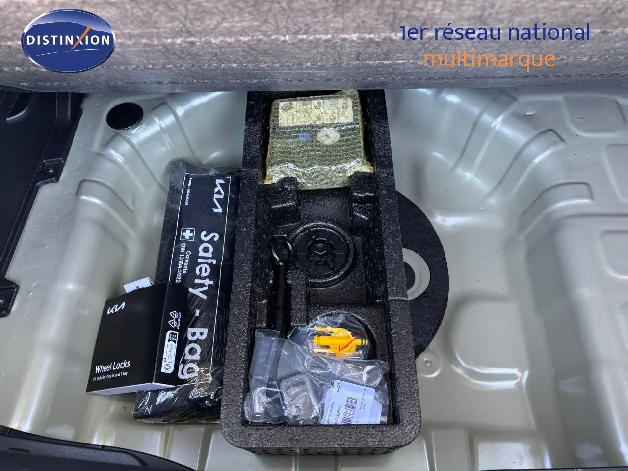 Coffre ouvert du Kia Stonic gris météore 2024 montrant rangement sous plancher avec kit de sécurité et outils.