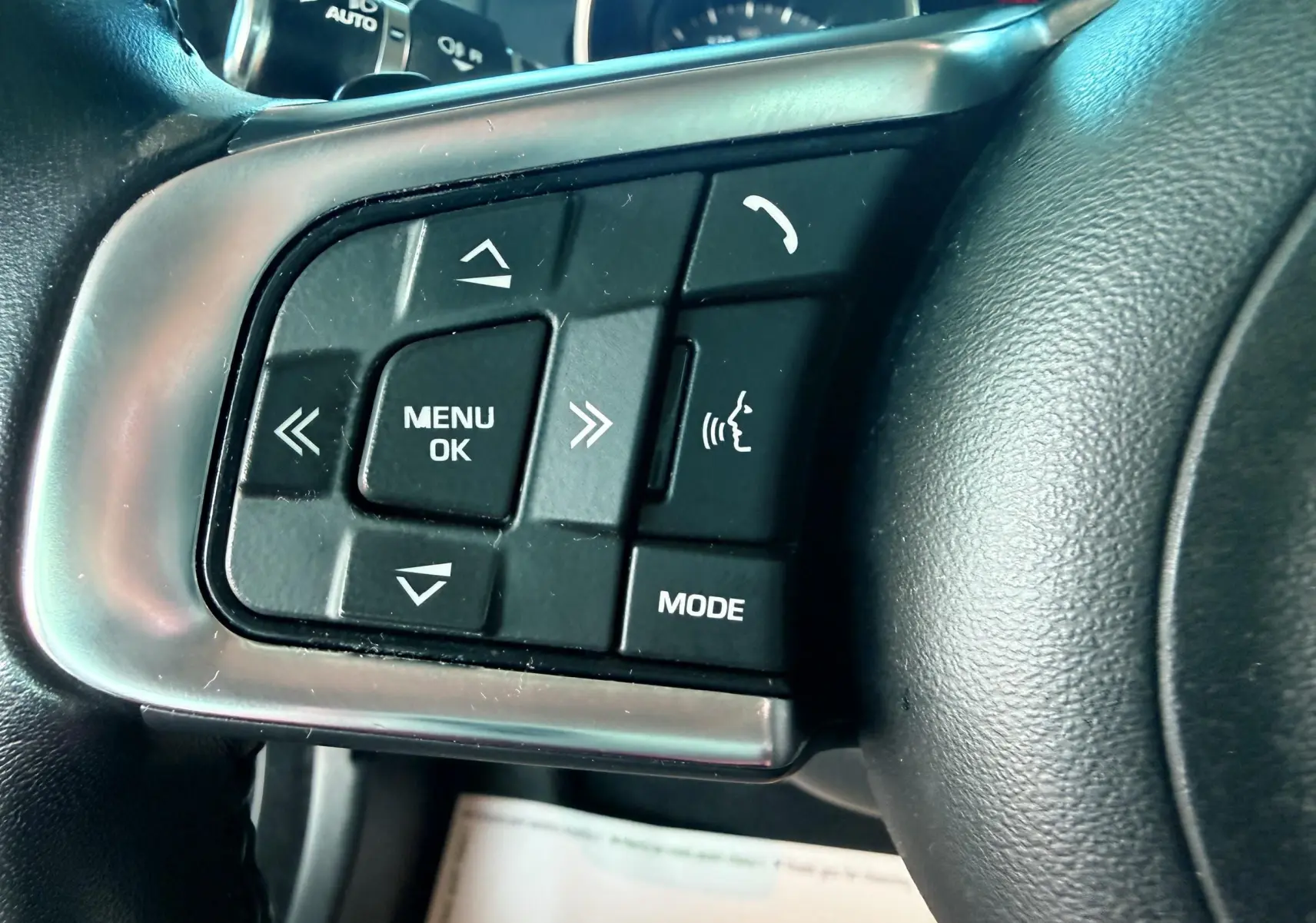 Gros plan sur les commandes du volant côté gauche de la Jaguar XE 2019, boutons noirs avec inscriptions blanches.