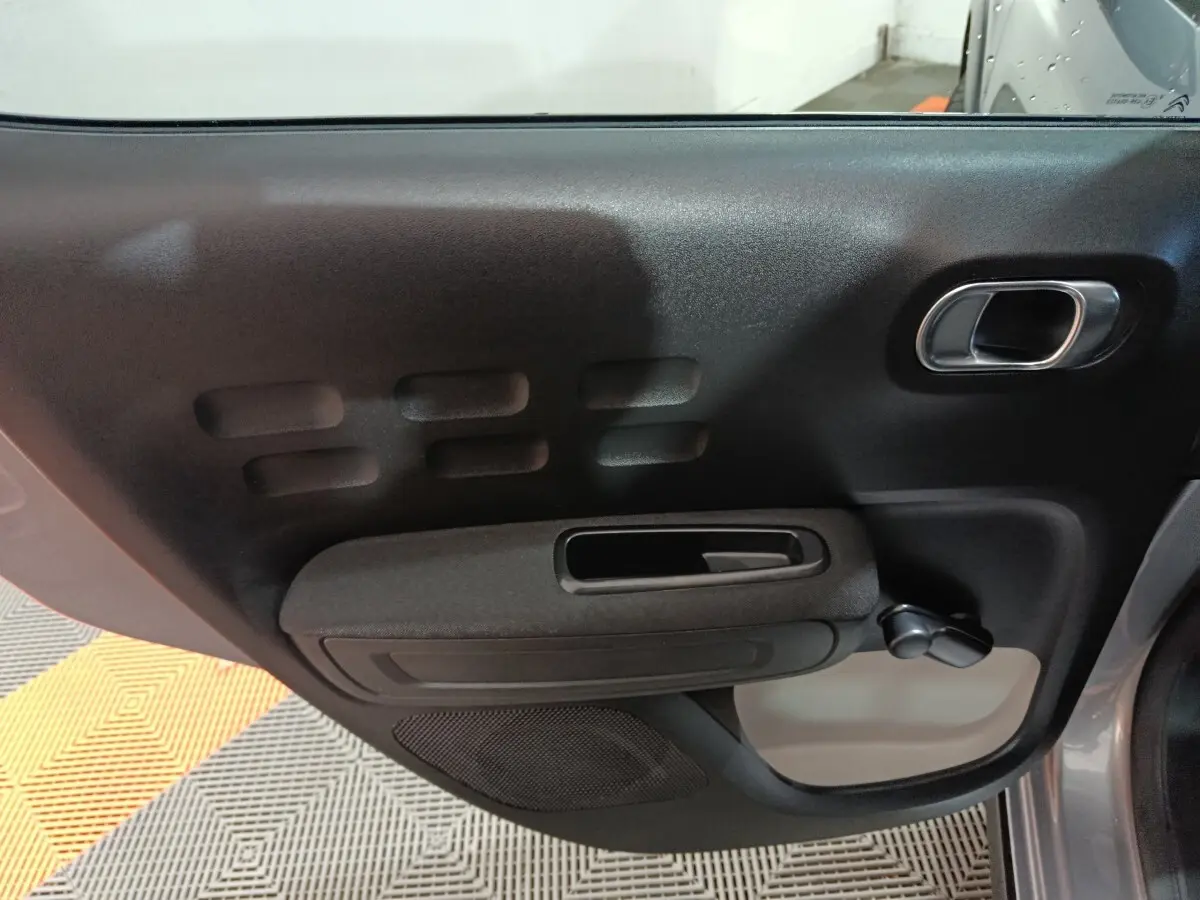 Vue rapprochée de la porte arrière droite gris foncé de la Citroën C3 avec poignée et manivelle de vitre manuelle.