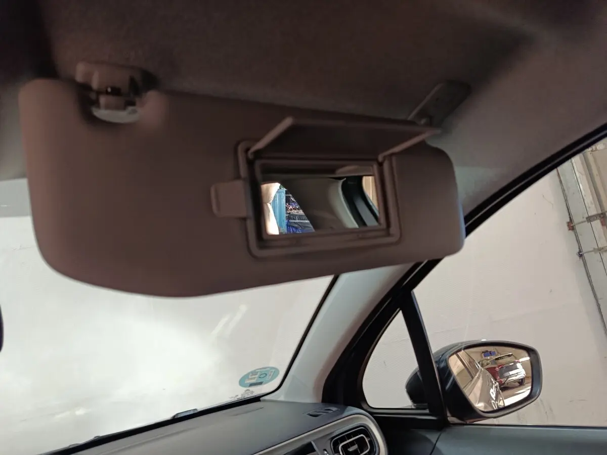 Vue intérieure côté conducteur sur le pare-soleil gris avec miroir intégré et rétroviseur extérieur noir d'une Citroën C3 gris foncé.