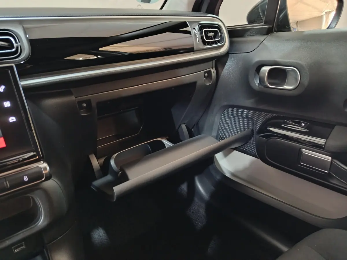 Intérieur côté passager de la Citroën C3 gris foncé 2024, boîte à gants ouverte et tableau de bord noir brillant.
