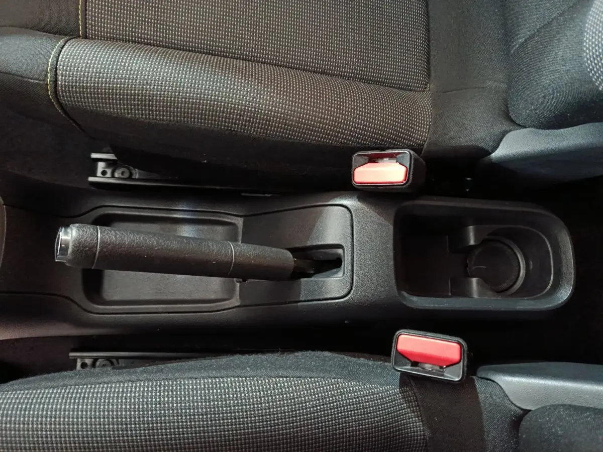 Vue plongeante sur la console centrale noire de la Citroën C3 2024, avec frein à main manuel et ceintures rouges.