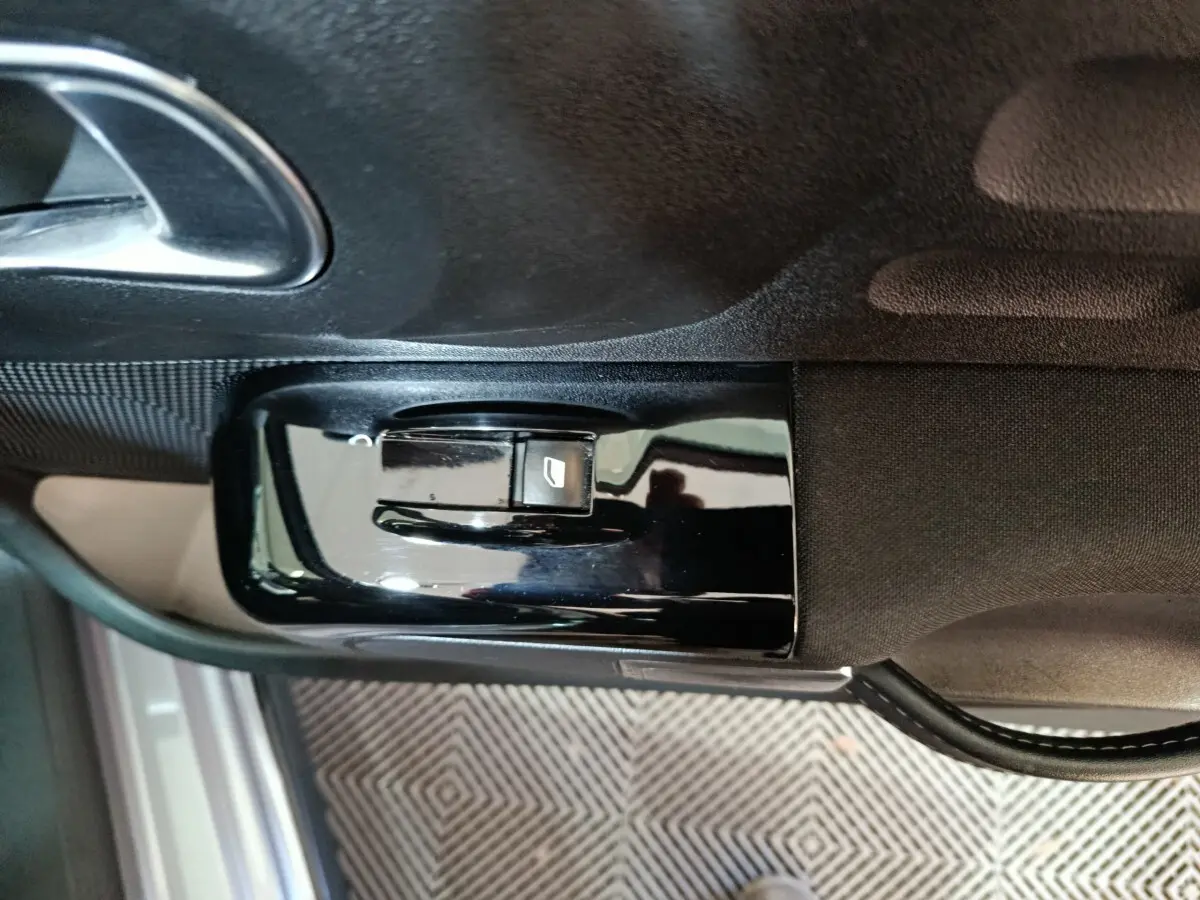 Gros plan sur la commande de lève-vitre côté conducteur d'une Citroën C3 gris foncé, avec poignée de porte visible.