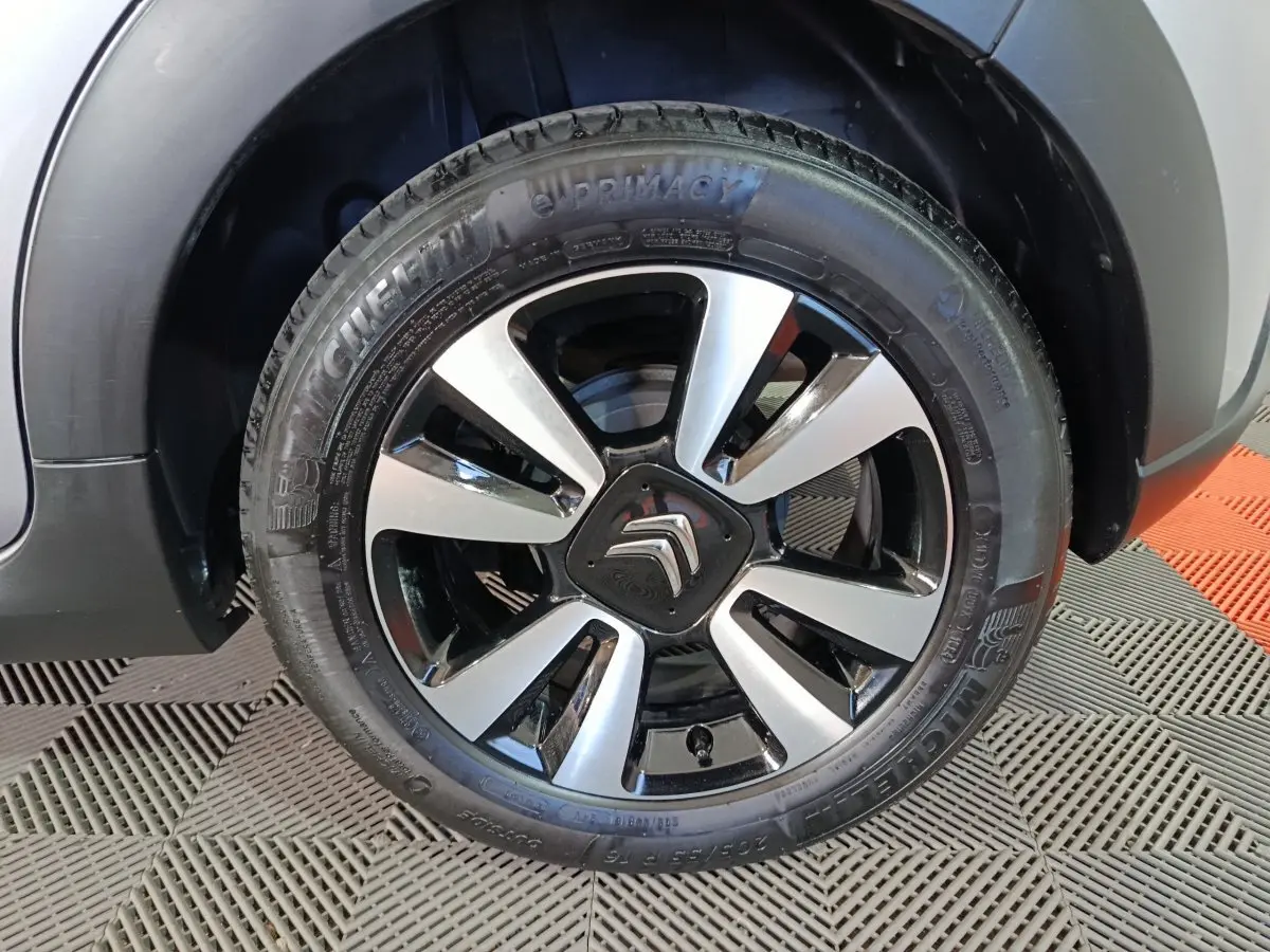 Gros plan sur la roue avant gauche d'une Citroën C3 gris foncé avec jante alliage bicolore et pneu Michelin.