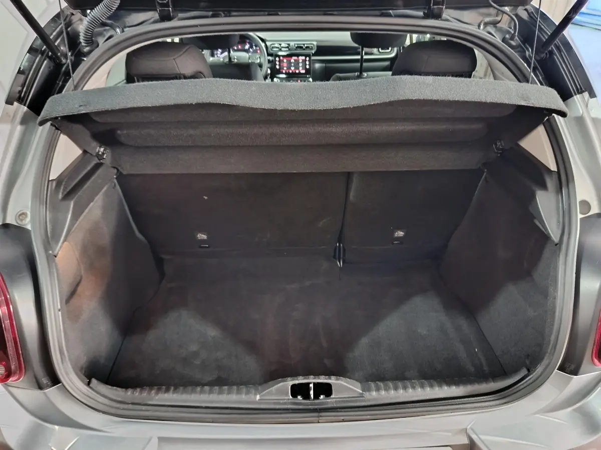 Coffre ouvert vu de l'arrière d'une Citroën C3 gris foncé 2024, intérieur noir et tablette de coffre relevée.