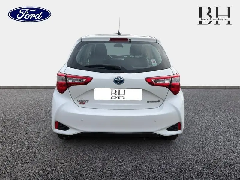 Vue arrière d'une Toyota Yaris 116h hybride blanche, avec feux arrière LED et logo Toyota bien visibles.