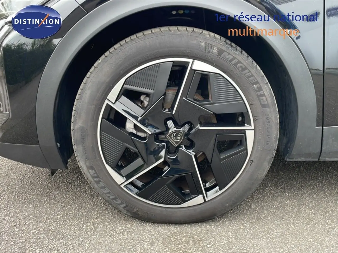 Gros plan sur la roue avant droite noire métal d'une Peugeot 408 Hybrid 145ch avec jante au design moderne bicolore.