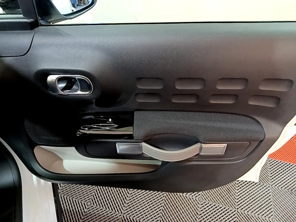 Vue rapprochée de la porte côté conducteur d'une Citroën C3 blanche, avec poignée intérieure en cuir et inserts noirs.