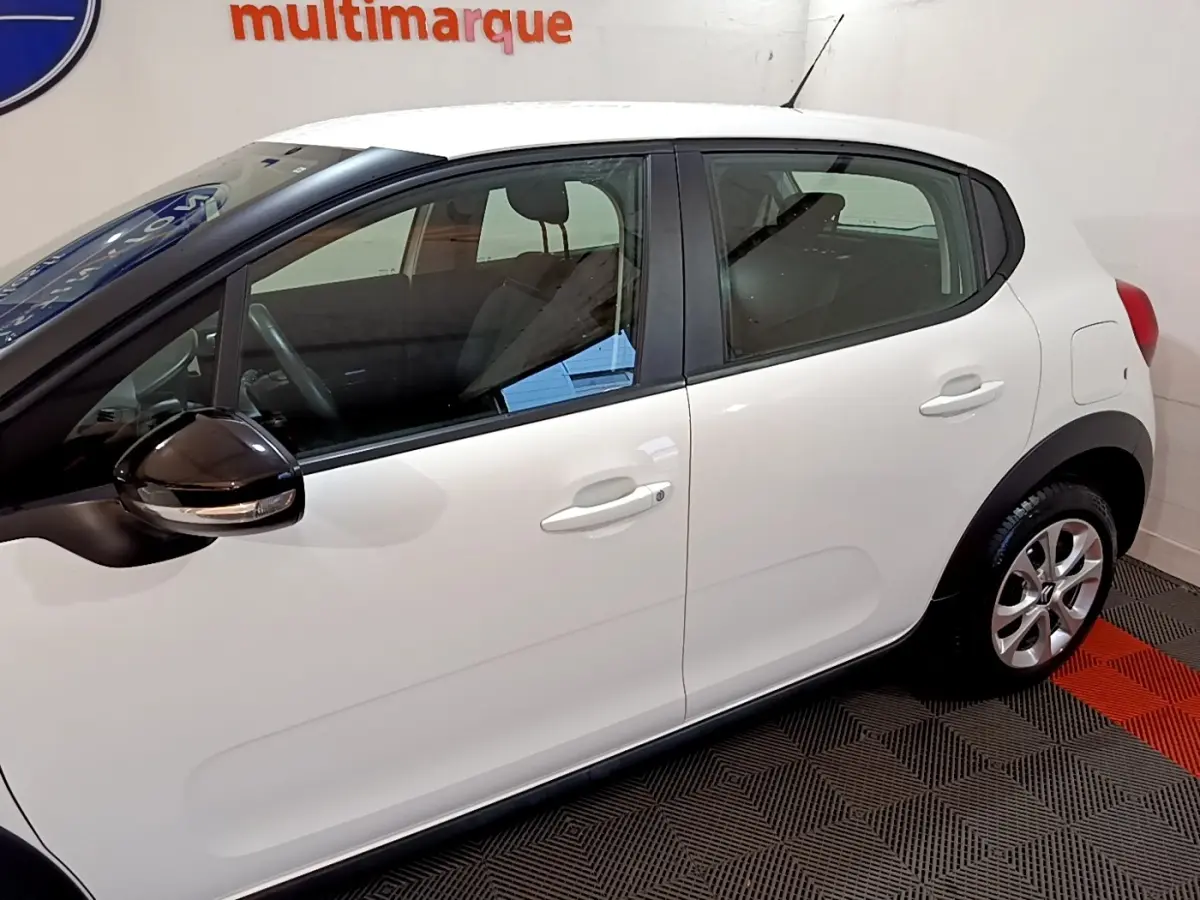 Vue latérale droite d'une Citroën C3 blanche avec rétroviseur noir brillant et jantes alliage en intérieur showroom.