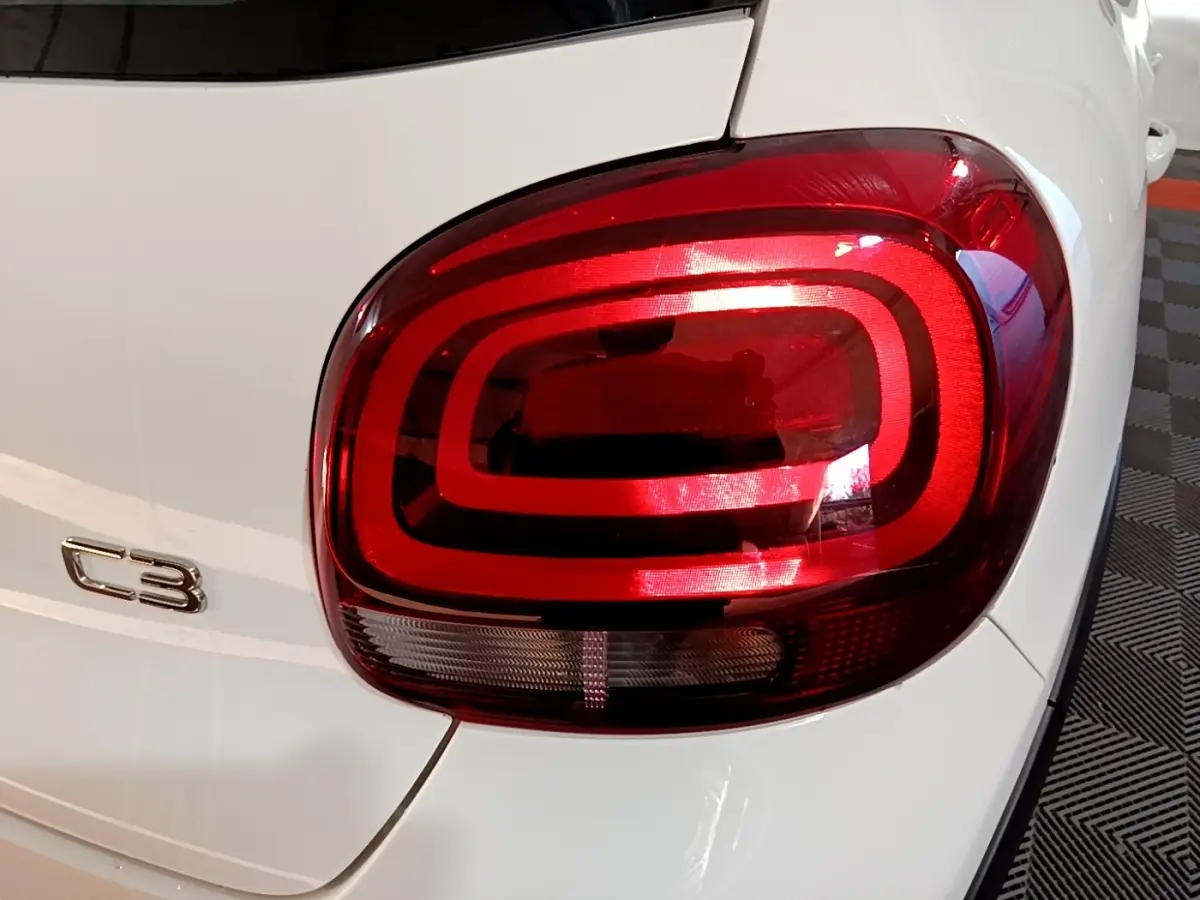 Gros plan sur le feu arrière droit rouge et le logo C3 d'une Citroën C3 blanche vue de l'arrière.