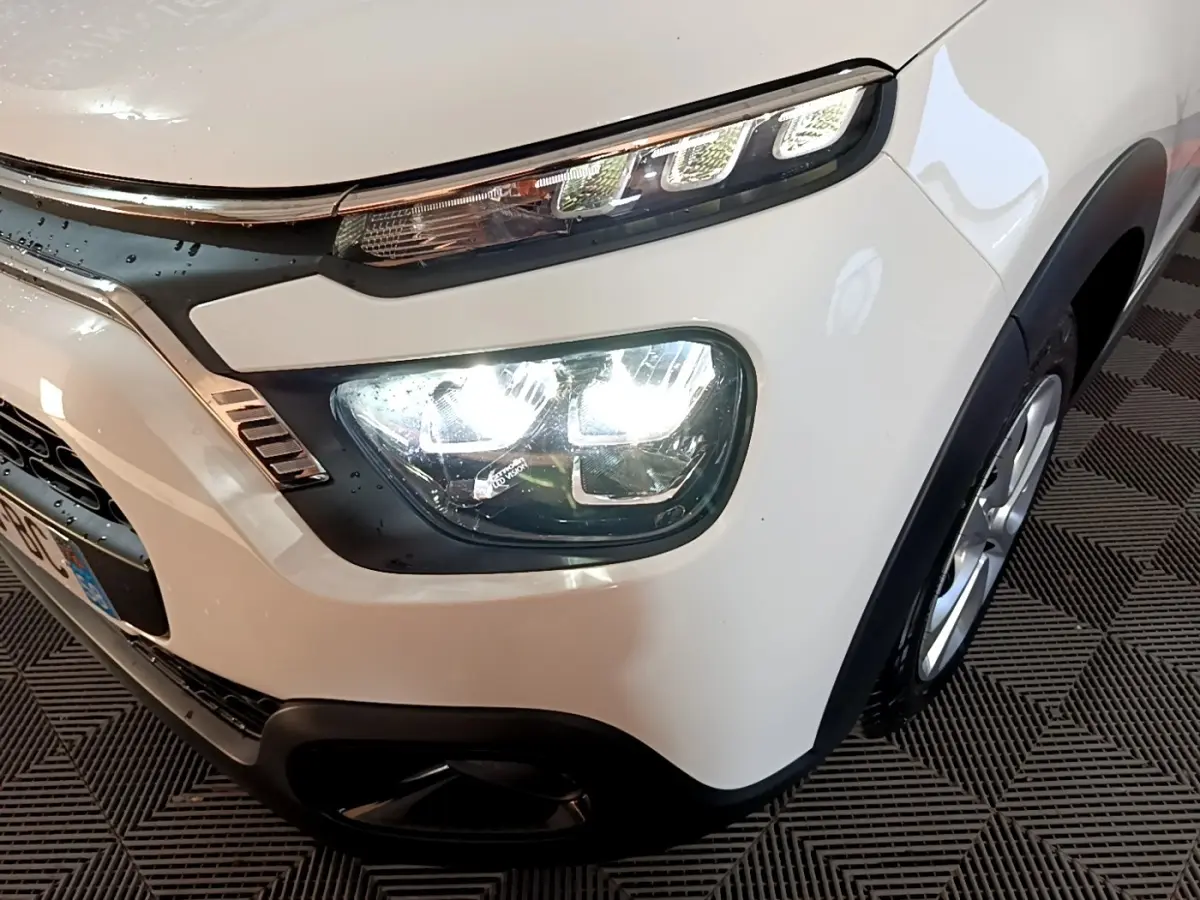 Gros plan sur l'avant droit d'une Citroën C3 blanche, mettant en valeur ses phares LED et son pare-chocs noir.