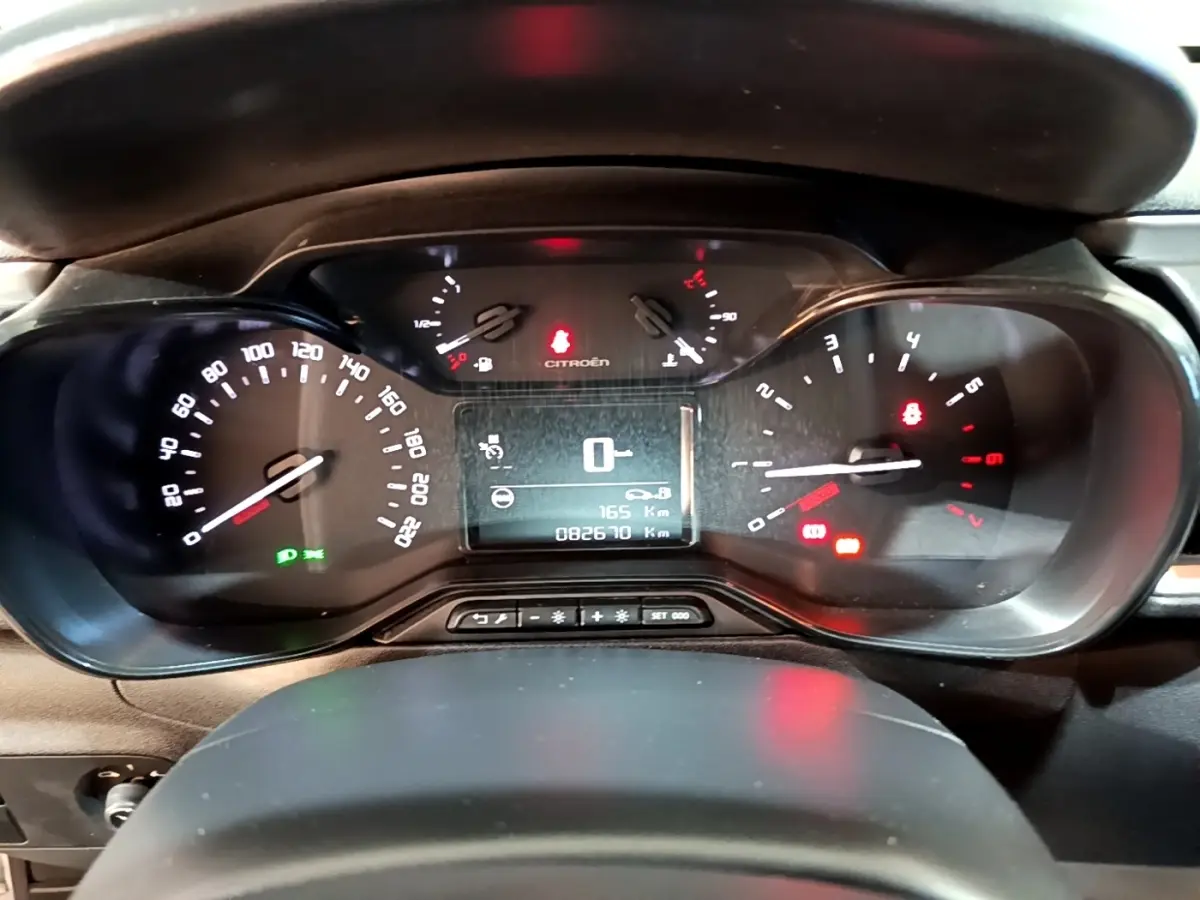 Vue rapprochée du tableau de bord numérique de la Citroën C3 blanche, affichant la vitesse à zéro et divers voyants allumés.