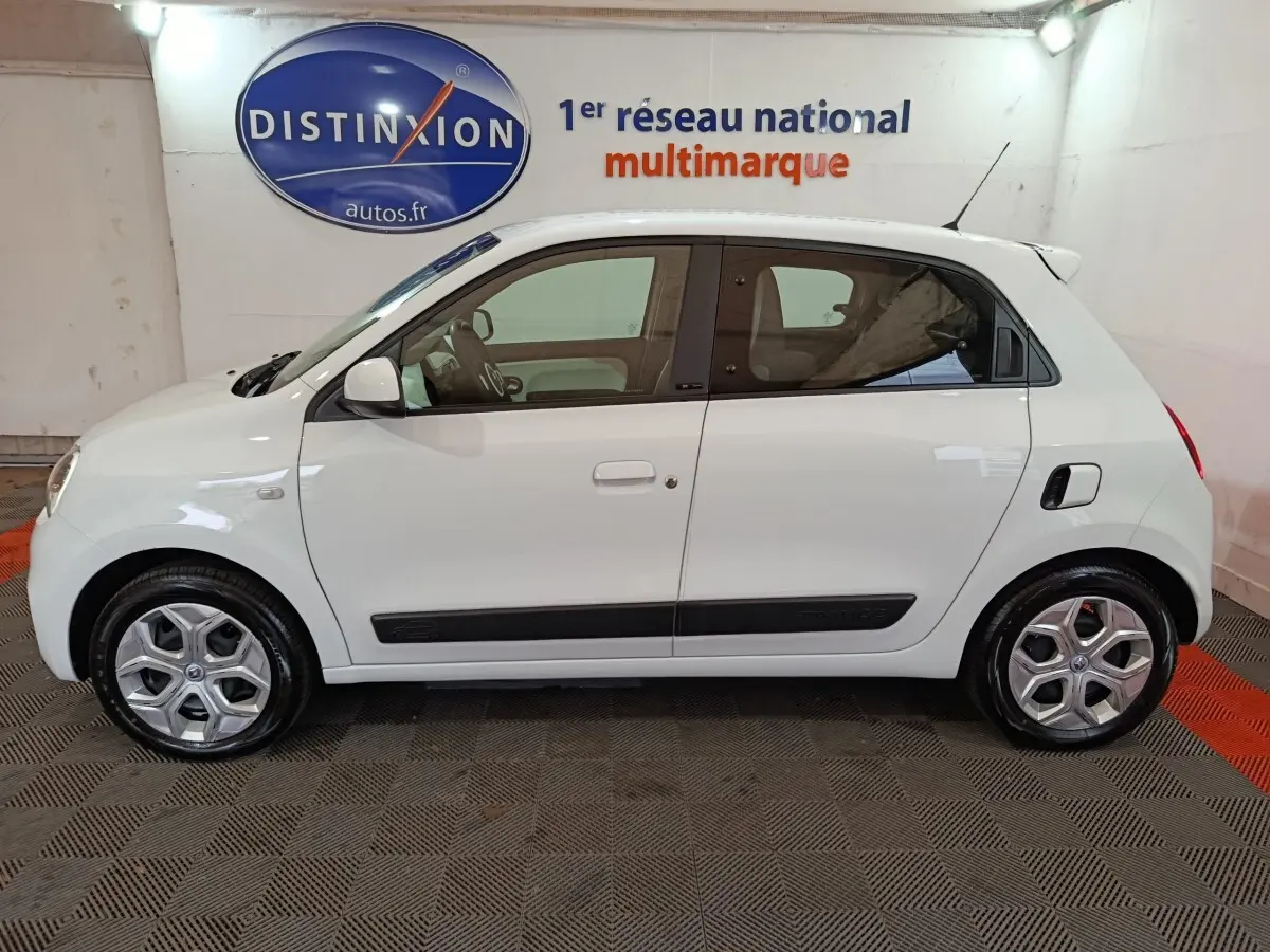 Profil latéral droit d'une Renault Twingo Zen blanche de 2021 avec poignées et rétroviseurs assortis, en intérieur showroom.