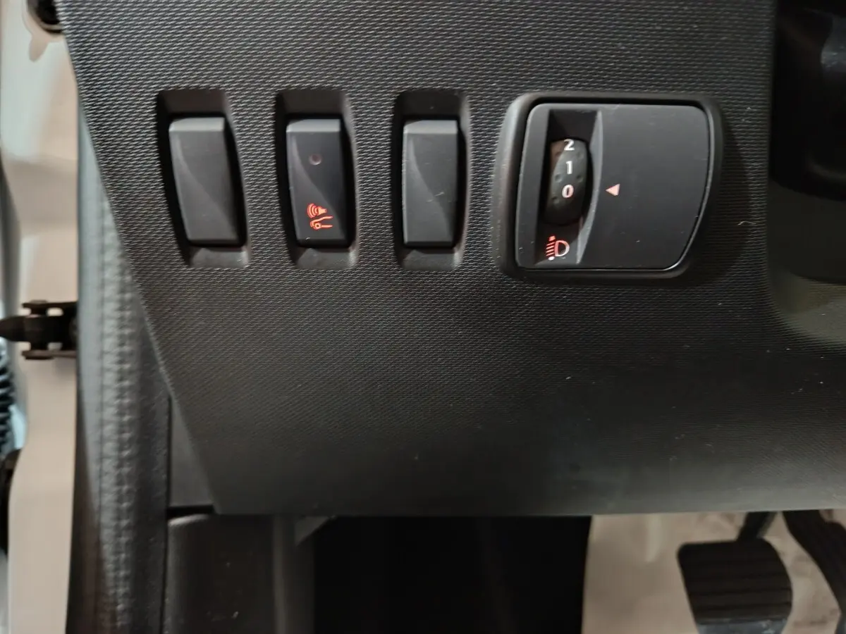 Détail des commandes d'éclairage et d'alerte sonore sur le tableau de bord côté gauche d'une Renault Twingo Zen blanche.