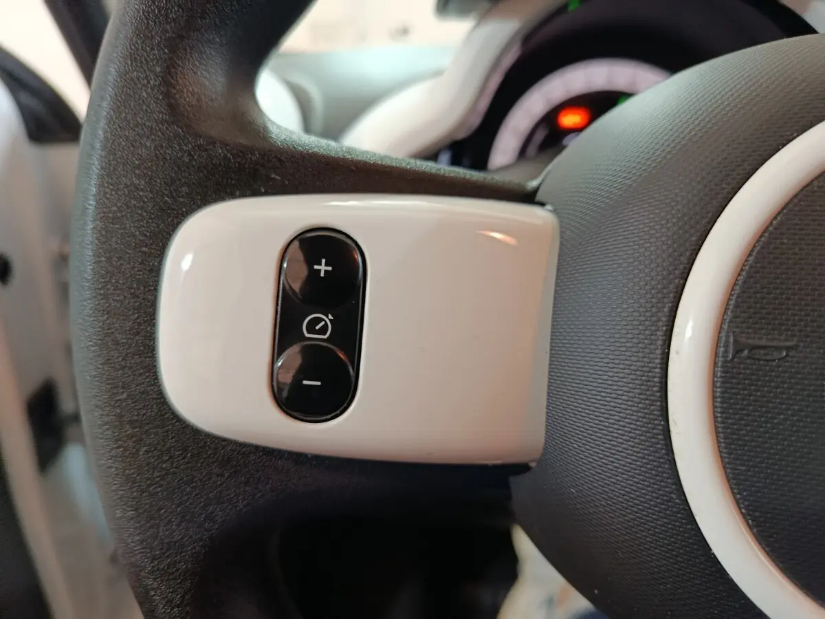 Gros plan sur les commandes blanches du régulateur de vitesse au volant d’une Renault Twingo Zen blanc électrique.