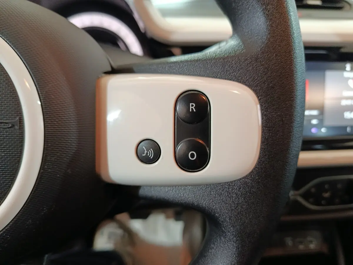 Gros plan sur les commandes blanches et noires du volant d'une Renault Twingo électrique blanche, tableau de bord flou en arrière-plan.