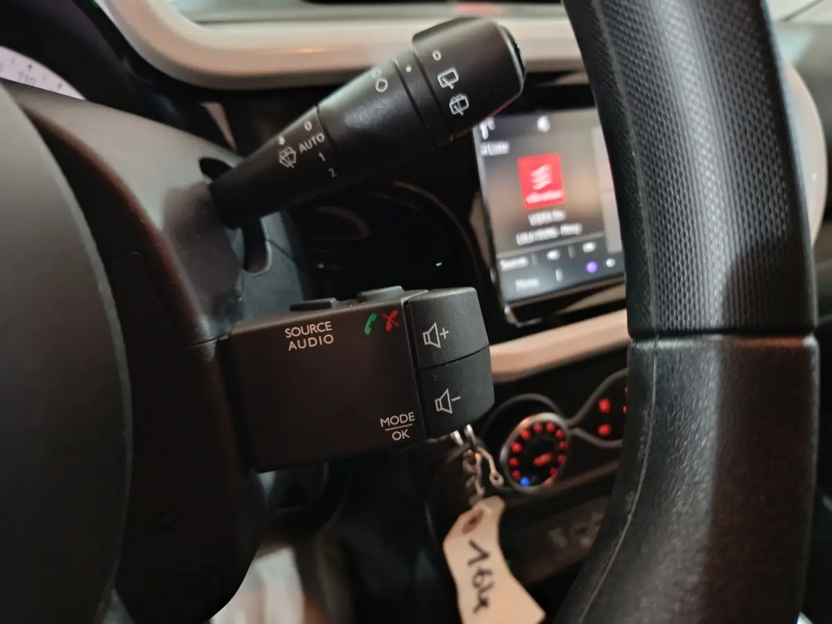 Gros plan sur la commande audio au volant d’une Renault Twingo blanche, avec écran tactile et commandes de climatisation en arrière-plan.